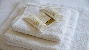 Toallas blancas dobladas con cuidado y dos botellas de jabón AURA sobre una cama.
