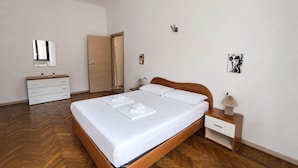 Une chambre à coucher avec un lit en bois, des tables de chevet blanches, une commode, un miroir et des œuvres d’art accrochées aux murs.