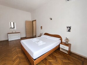 Ein Schlafzimmer mit einem Holzbett, weißen Nachttischen, einer Kommode, einem Spiegel und Kunstwerken an den Wänden.