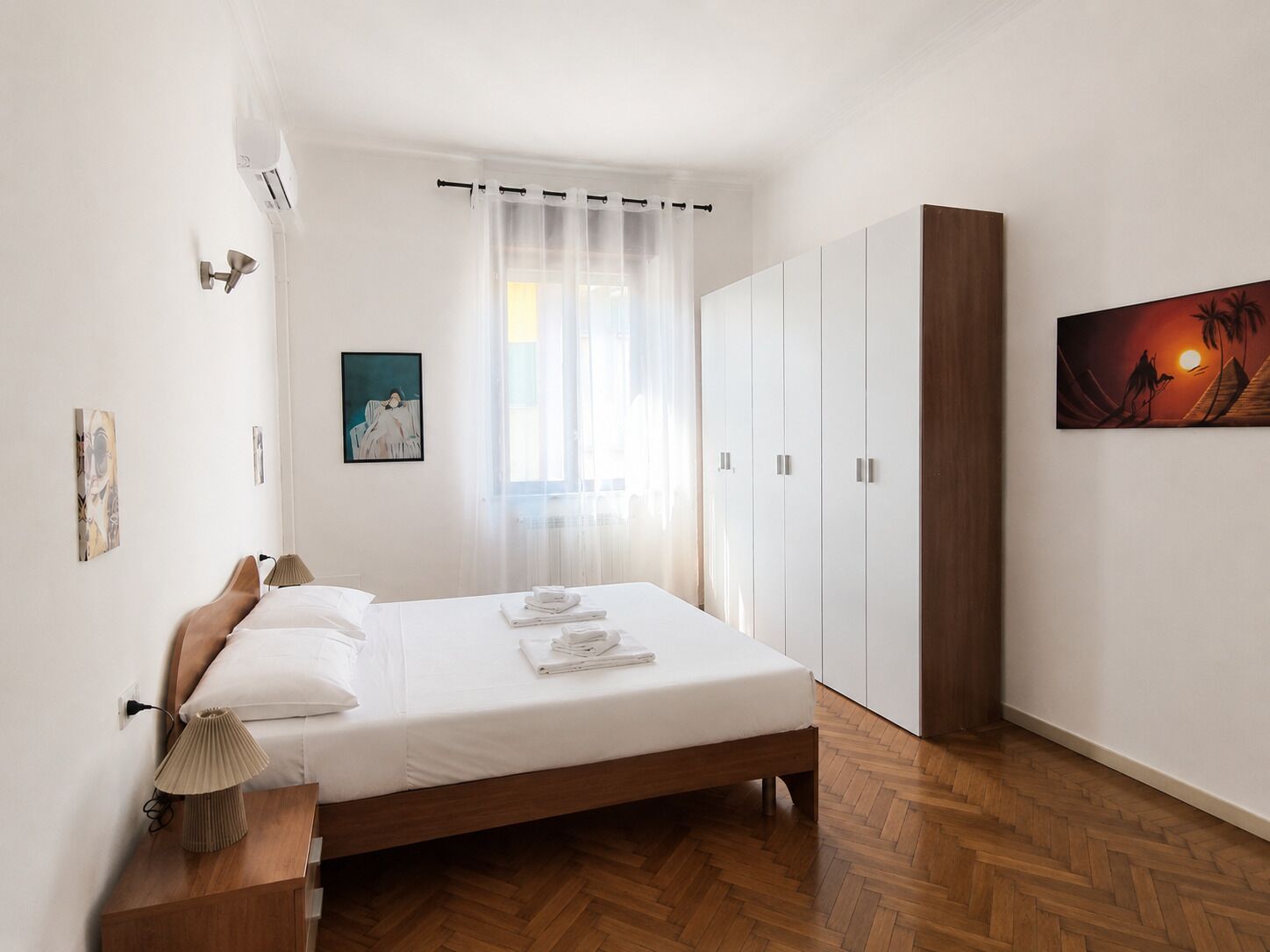 A bedroom with a bed, a wardrobe, a painting, and a window with curtains.