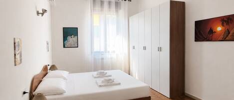 A bedroom with a bed, a wardrobe, a painting, and a window with curtains.