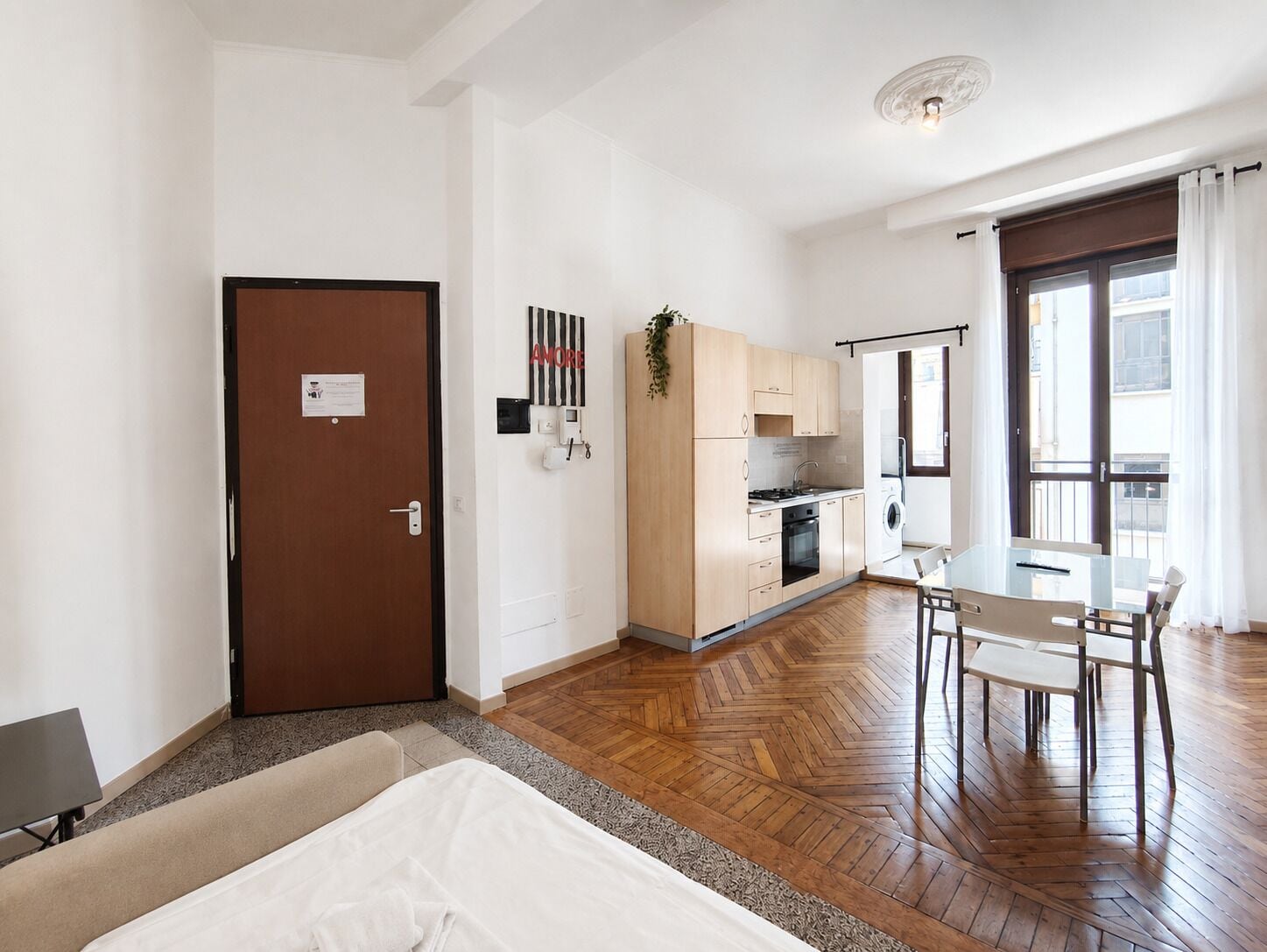 Quarto de hotel compacto com cama, cozinha compacta, área de refeições e uma janela grande.