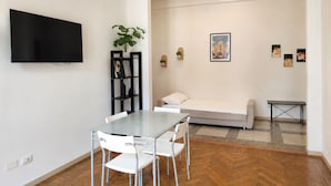 Un salon moderne comprenant une table à manger, des chaises, un canapé, un téléviseur et des œuvres d’art accrochées aux murs.