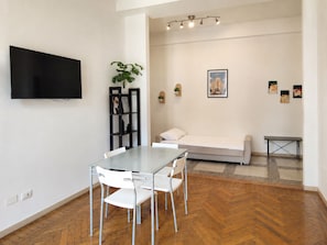Ein modernes Wohnzimmer mit Esstisch, Stühlen, einer Couch, einem Fernseher und Kunstwerken an den Wänden.
