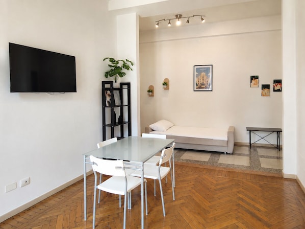 A modern living room with a dining table, chairs, a sofa, a TV, and artwork on the walls.