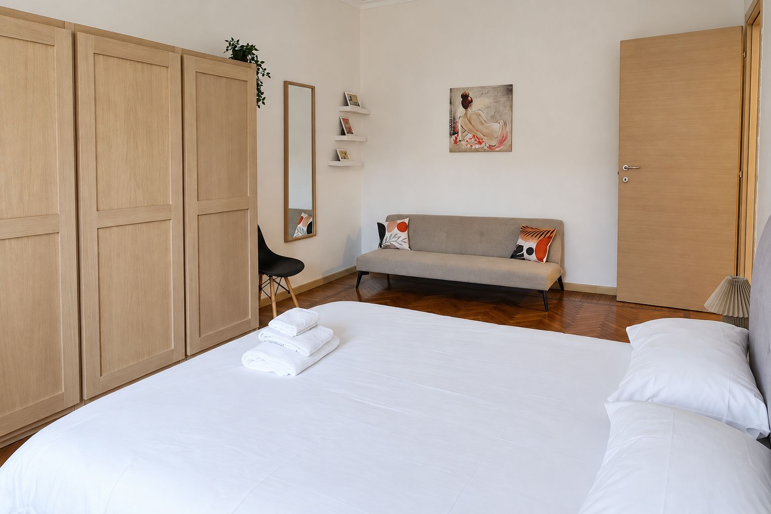 Une chambre d’hôtel avec un grand lit, un canapé, une armoire, un miroir et un tableau au mur.