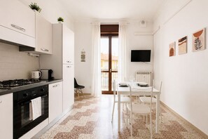 A modern kitchen with a stove, oven, and white cabinets. There is a dining area with a table and chairs, and a TV mounted on the wall. - BIG Living Goldoni [Duomo–M4–Linate] (Milan)