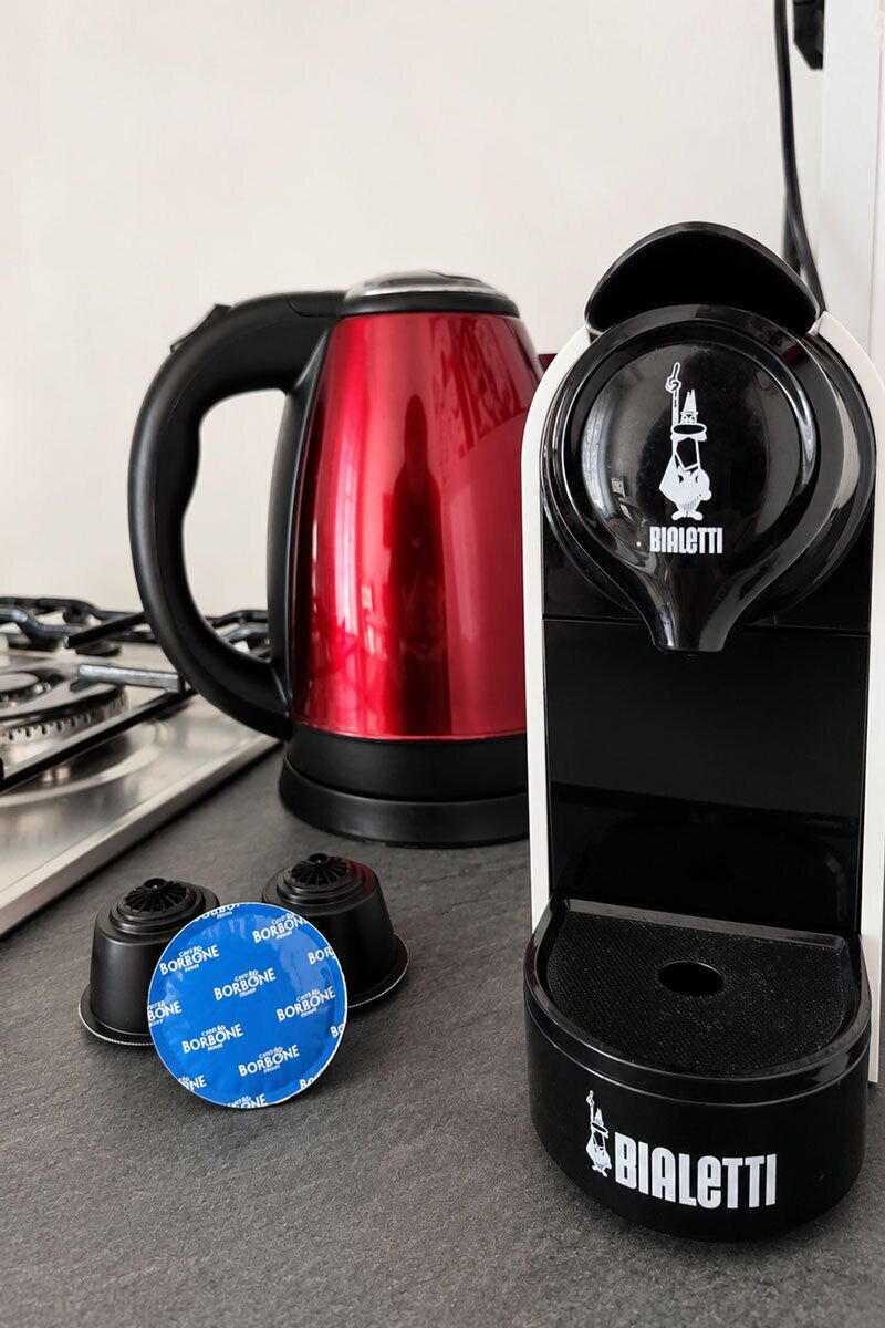 A kitchen with a red kettle, a black electric kettle, and a Bialetti brand coffee capsule.