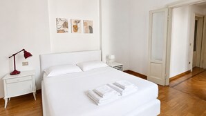 Ein Hotelzimmer mit einem Bett, einem Nachttisch, einer Lampe und einer Wand mit Kunstwerken.