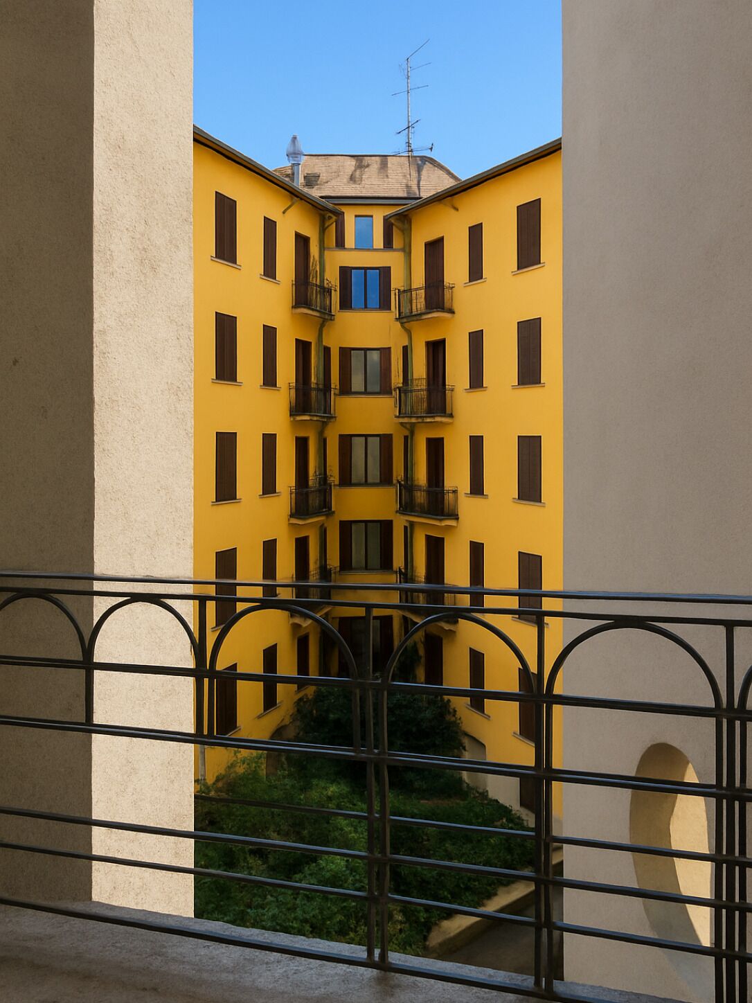 Un bâtiment jaune doté de nombreux balcons et fenêtres, vu depuis un balcon orné d’une rambarde en métal.
