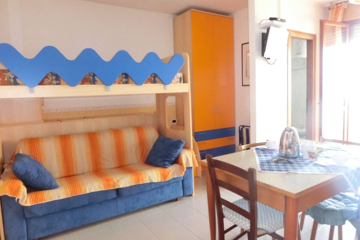 A room with a bunk bed, a sofa, a table with a kettle, and a cabinet.