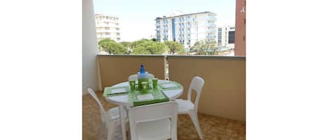A small balcony with a round table and four white chairs, a blue water bottle, and green placemats.