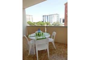 Uma varanda com uma mesa redonda e quatro cadeiras brancas, uma garrafa de água azul e jogos americanos verdes.