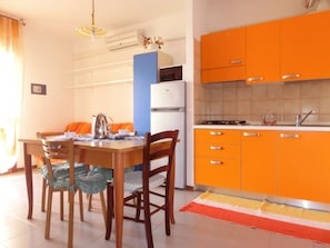 Una cocina compacta con armarios color naranja, un refrigerador blanco y una mesa de comedor con sillas.