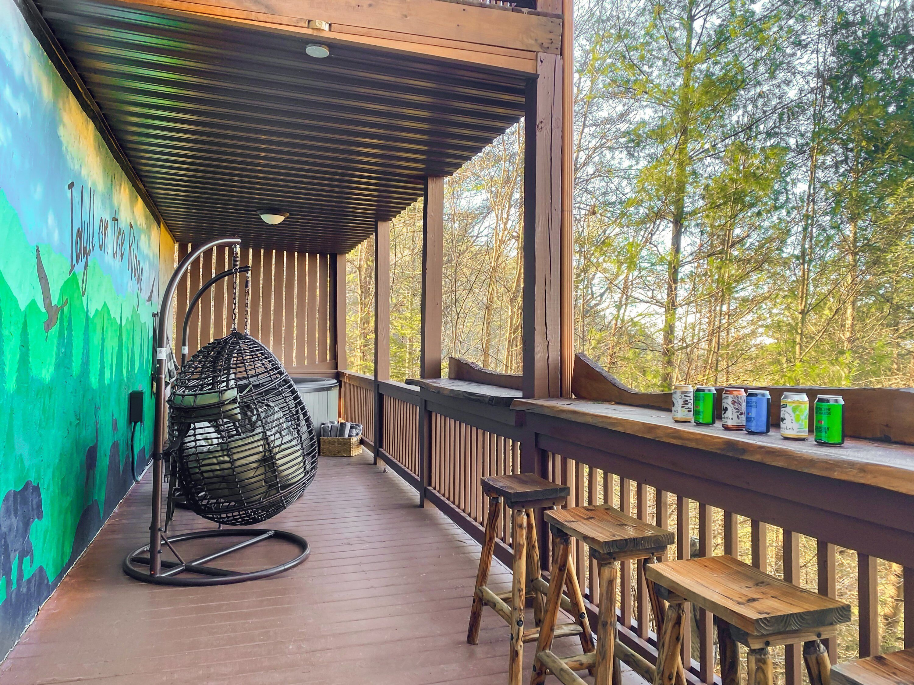 A wooden deck with a hanging chair, a bar stool, and a railing with cans of beverages.