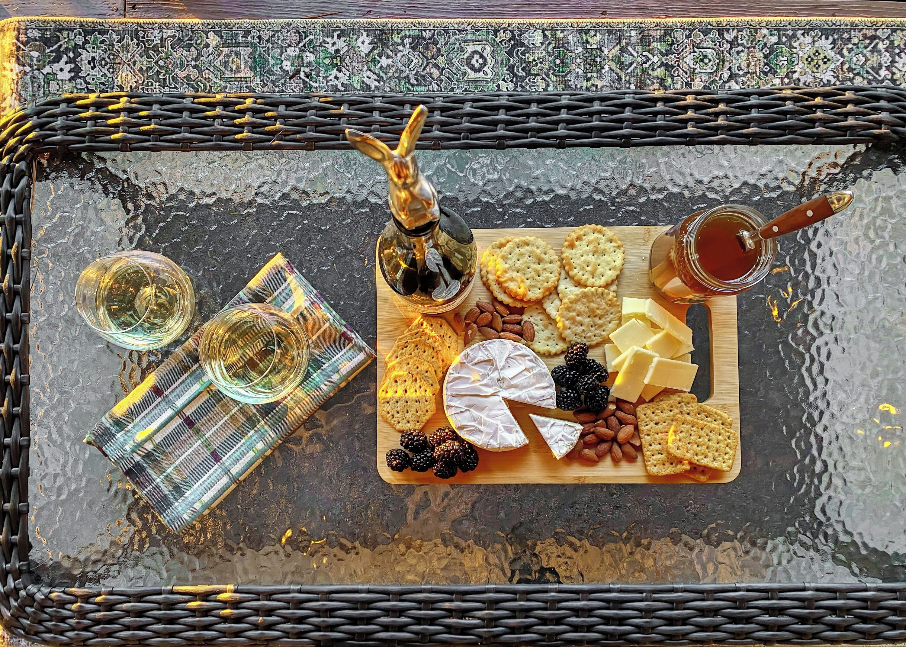 Una tabla de embutidos con queso, galletas, almendras y frambuesas sobre una mesa de vidrio.