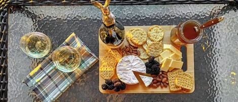 Una tabla de embutidos con queso, galletas, almendras y frambuesas sobre una mesa de vidrio.