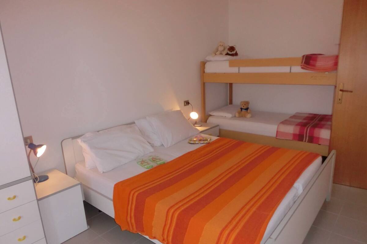 Ein Schlafzimmer mit Etagenbett, einem Einzelbett, einem Nachttisch mit Lampe und einer Kommode mit Schubladen.