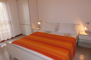 Un dormitorio con cama, cortinas blancas, armario y lámparas de noche.