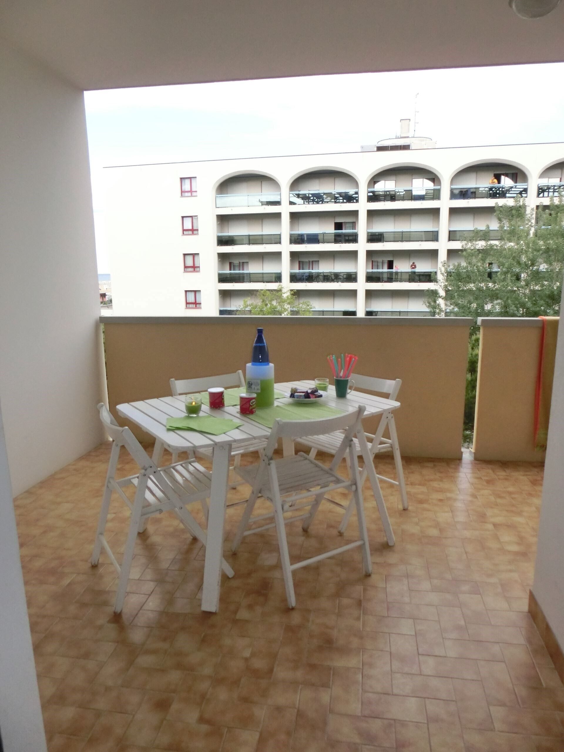 A balcony with a white table and chairs, a bottle, and a cup.
