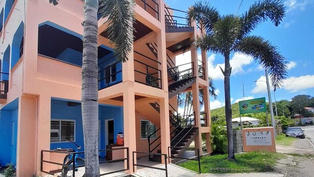 Un edificio a più piani con balconi, palme e un cartello che indica un'attività commerciale.
