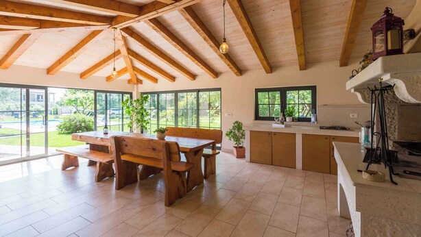A spacious kitchen with wooden beams, large windows, and a dining area with a wooden table and benches. - Holiday apartment With pool and large garden (Sveti Lovreč)