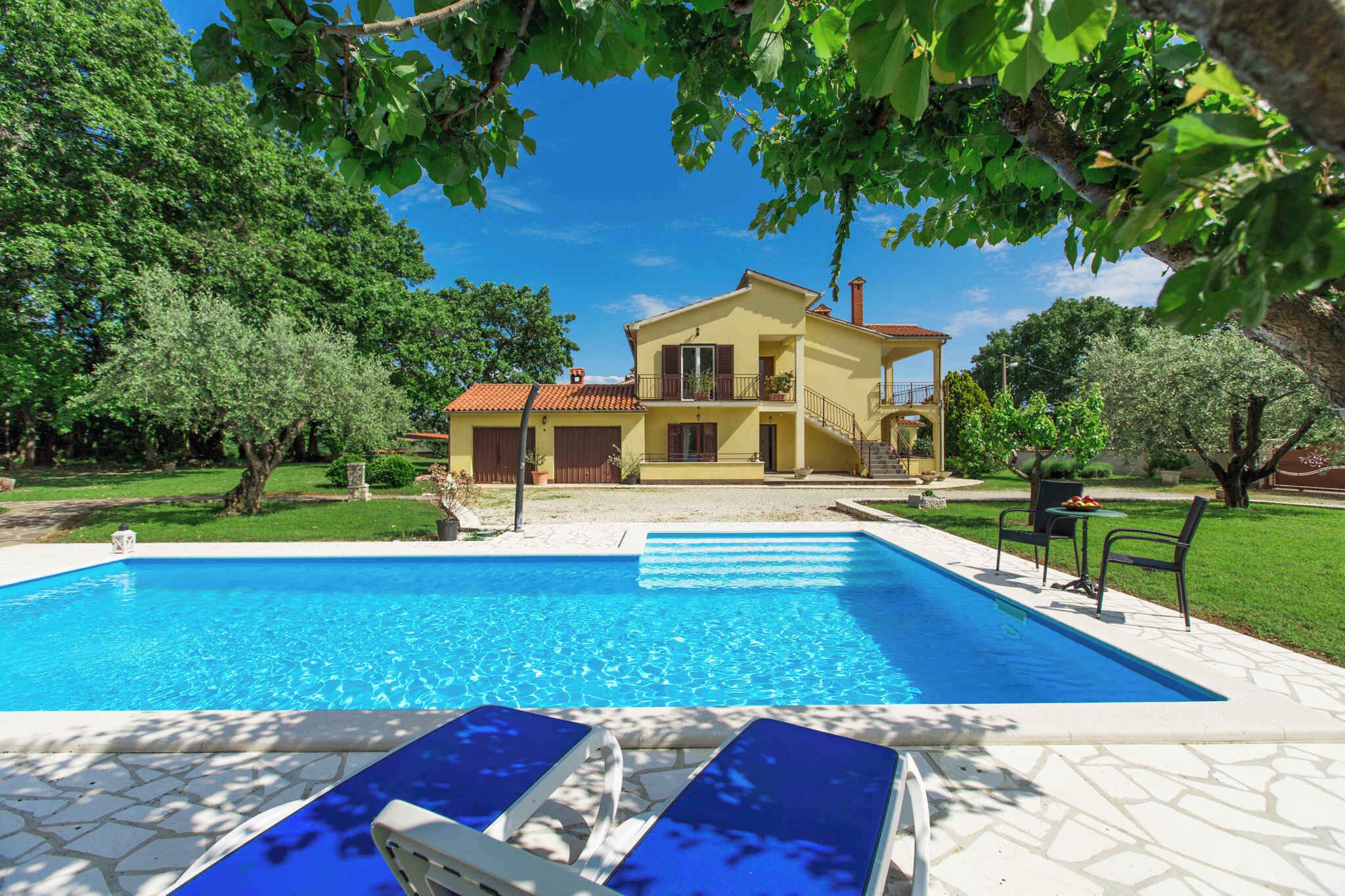 A swimming pool with lounge chairs, a yellow house with a balcony, and surrounding greenery.