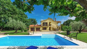 A swimming pool with lounge chairs, a yellow house with a balcony, and surrounding greenery. - Holiday apartment With pool and large garden (Sveti Lovreč)