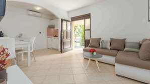 A modern living room with a sofa, a dining table with chairs, and a kitchen area visible through an open doorway. - Holiday apartment With pool and large garden (Sveti Lovreč)