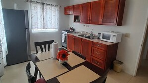 Une cuisine compacte dotée de meubles en bois, d’une cuisinière à gaz, d’un four à micro-ondes et d’un coin repas avec une table et des chaises.