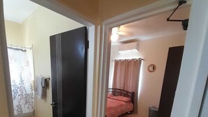 Une chambre à coucher avec un lit, une fenêtre avec des rideaux, une table de chevet et un climatiseur fixé au mur.