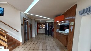 A hotel corridor with hexagonal patterned flooring, a wooden staircase, an elevator, and a reception area with a counter and informational signs. - HOTEL SAN THOMAS INN (Panama City)
