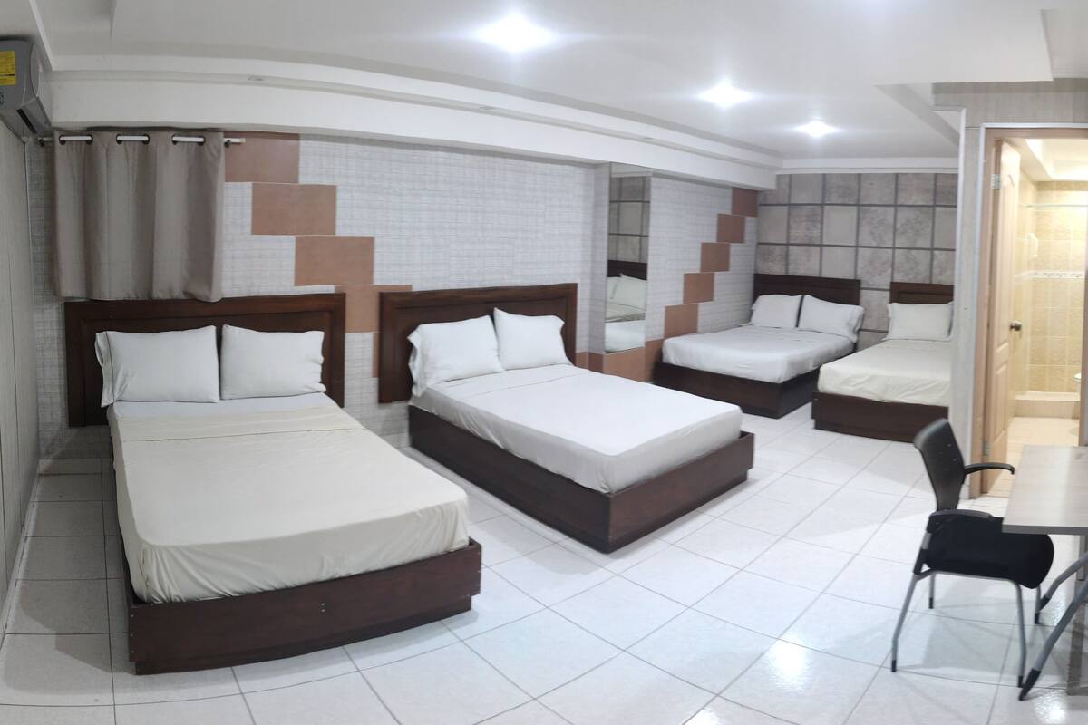 Une chambre d’hôtel avec trois lits, un bureau et une chaise.