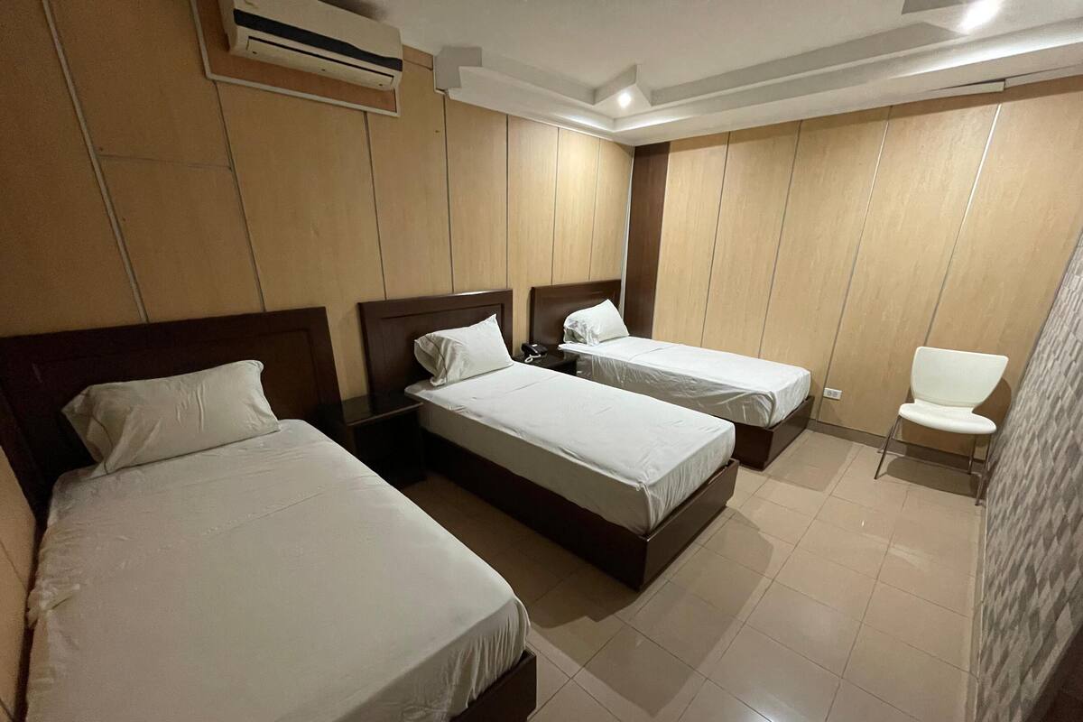 Une chambre d’hôtel avec deux lits simples, une table de chevet avec un téléphone et une chaise blanche.