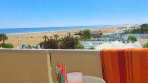 Une table avec une boisson, des serviettes et un porte-gobelet, placée sur un balcon donnant sur une plage.