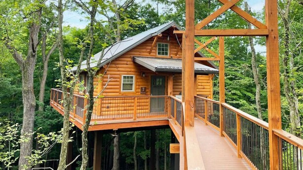 Eine Holzhütte mit Balkon und einer Holzterrasse, umgeben von Bäumen.