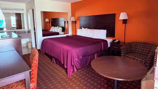 Une chambre d’hôtel avec un lit, un bureau, une chaise, une table ronde et un miroir.