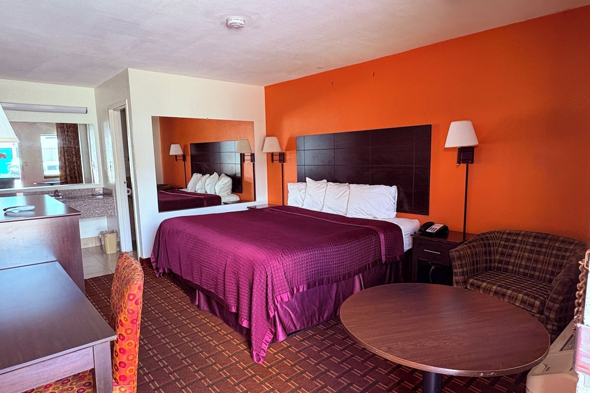 A hotel room with a bed, a desk, a chair, a round table, and a mirror.