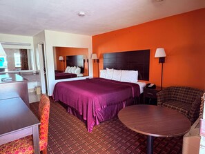 A hotel room with a bed, a desk, a chair, a round table, and a mirror. - Royal Regency Inn (Rock Hill)