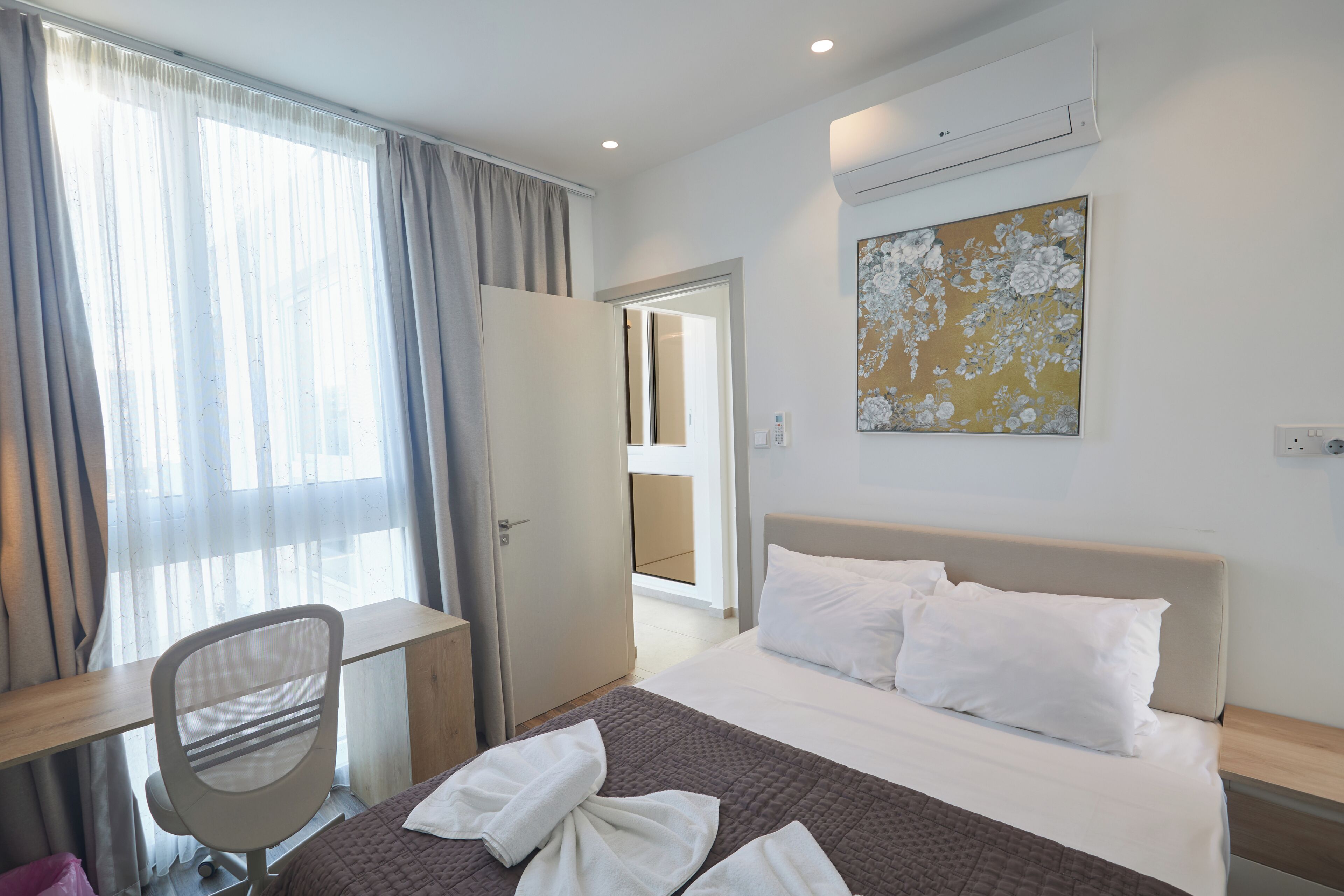 A hotel room with a bed, a desk, a chair, and a painting on the wall.