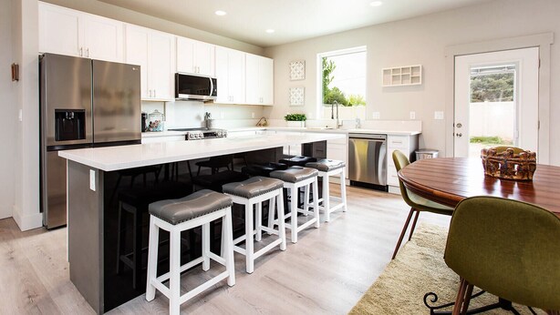 A modern kitchen with white cabinets, stainless steel appliances, and a central island with bar stools. - Brand Spankin' New 4 bedroom home Sleeps 8 Pet friendly (Kimberly)