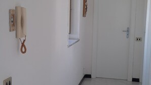 A hallway with white walls, a tiled floor, a white door at the end, and a wall-mounted air conditioning unit. - Palazzo Di Donna Penthouse terrace view Vesuvius strategic to Pompeii, Amalfi coast (Sant'Egidio del Monte Albino)