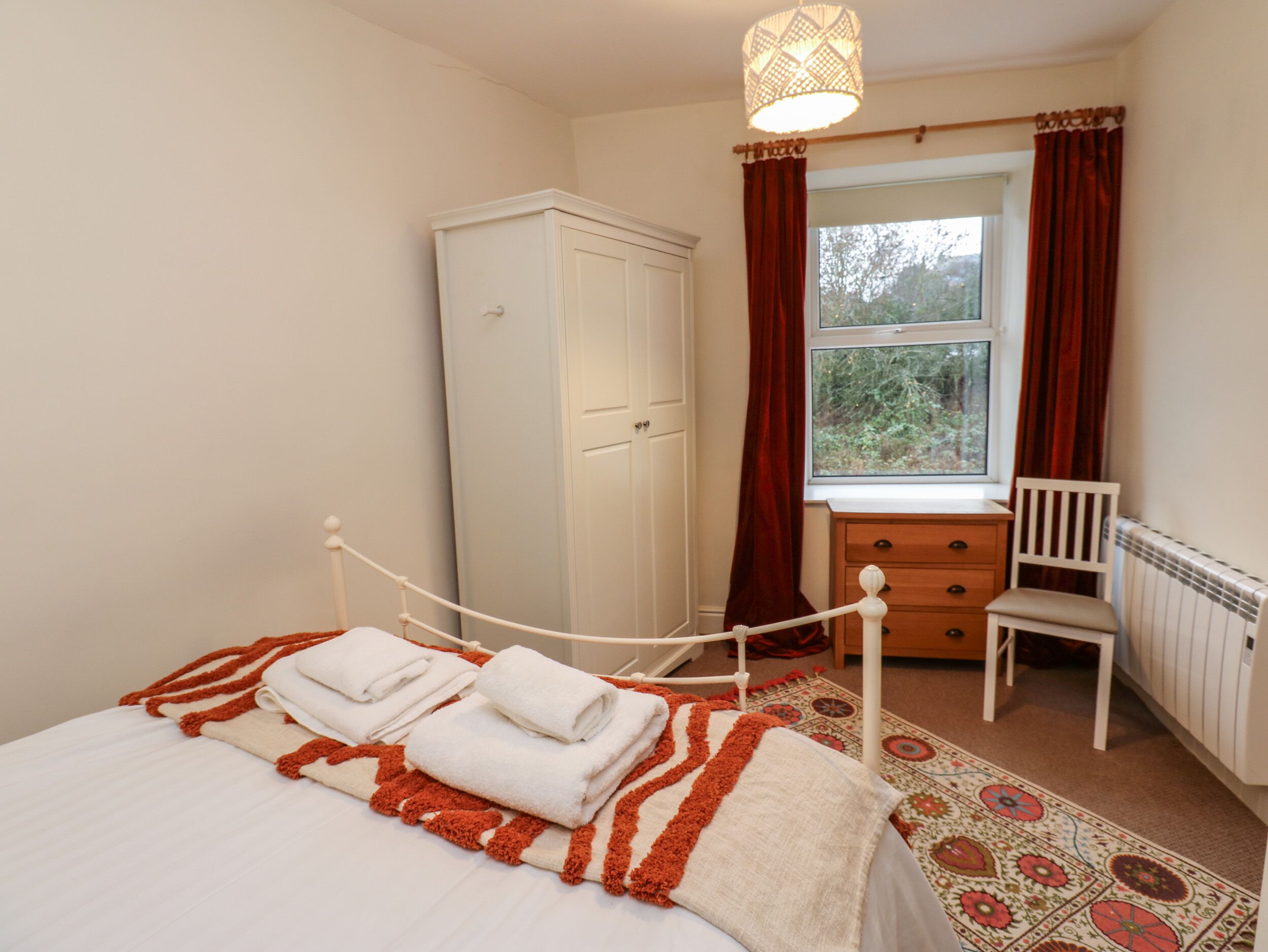 A bedroom with a bed, a wardrobe, a desk with a chair, and a window with curtains.