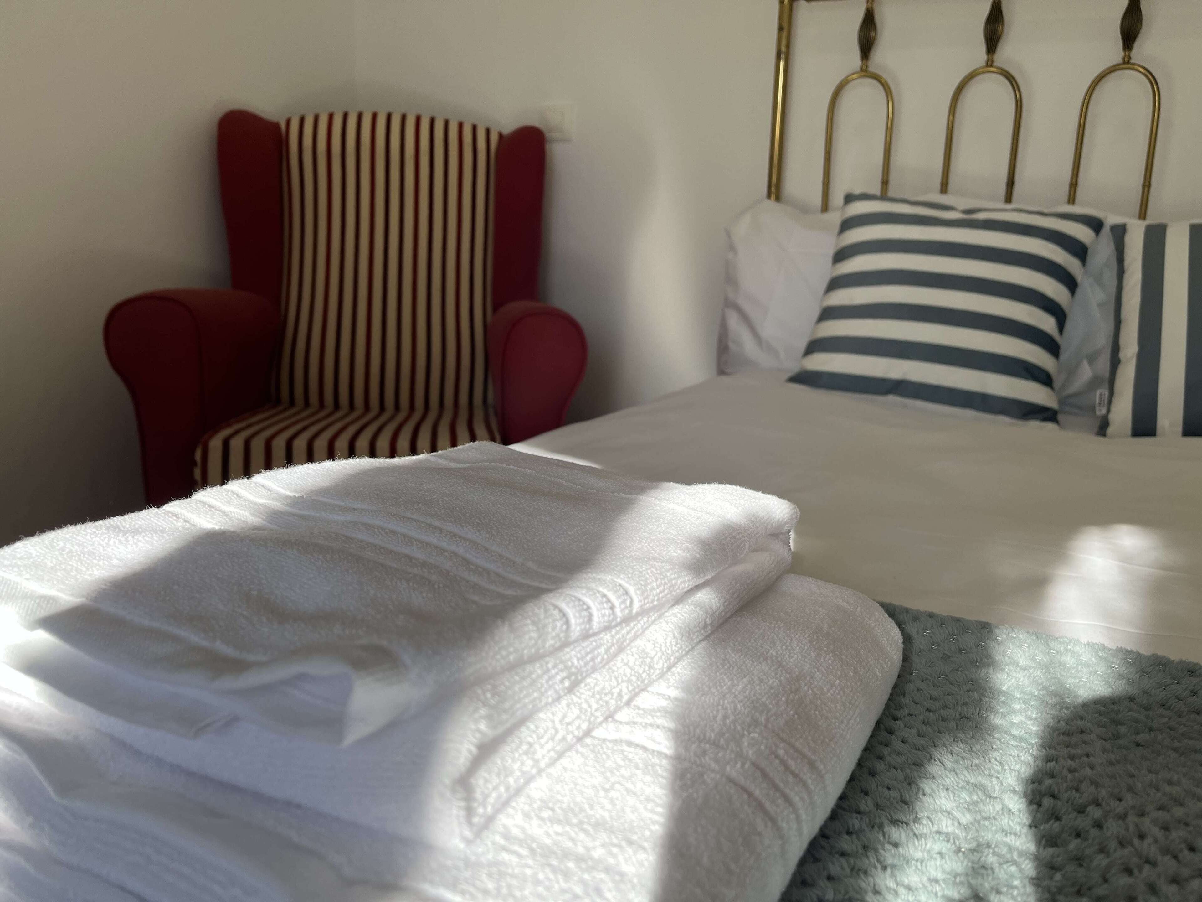 A neatly made bed with white linens, a striped armchair, and a headboard with metal finials.