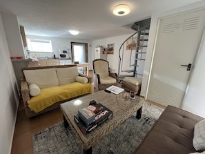 Cozy living space with a wicker sofa, armchair, and coffee table, featuring a spiral staircase and modern kitchen area.