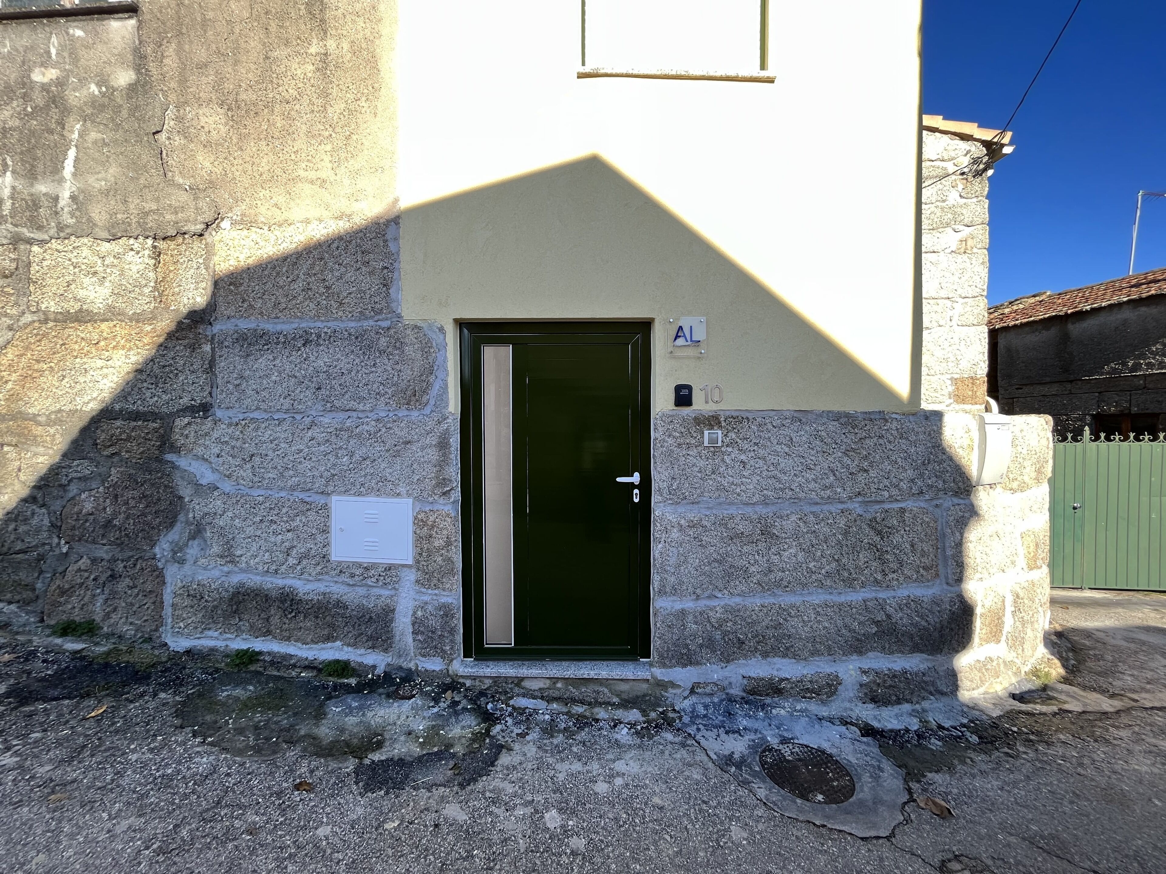 A stone building with a green door, a small sign above the door, and a number '10' on the wall.