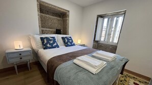 Ein Schlafzimmer mit einem Bett, Nachttischen, einem Wandregal, einem Fenster und einem gemusterten Teppich.