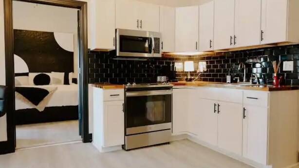 A modern kitchen with white cabinets, a black backsplash, stainless steel appliances, and a wooden countertop.