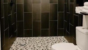 A modern bathroom with dark tiled walls, a patterned shower floor, and a white toilet.