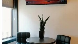 A room with a round table, two chairs, a potted plant, and a TV displaying a sunset scene.